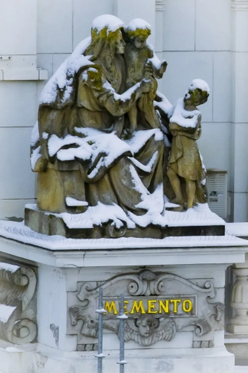 Snow-covered sculptural group above the glowing word MEMENTO